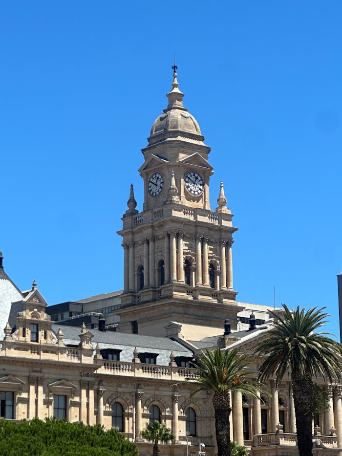 Iconic Cape Town City Hall with clock tower against a clear blue sky, featuring classic architecture and palm trees.