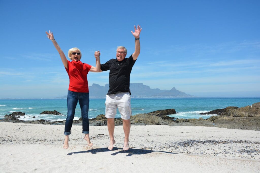Elderly couple jumping with joy on a beach in Cape Town with Table Mountain in the background.